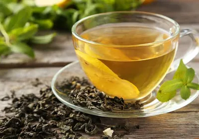 A glass cup of green tea next to loose green tea leaves